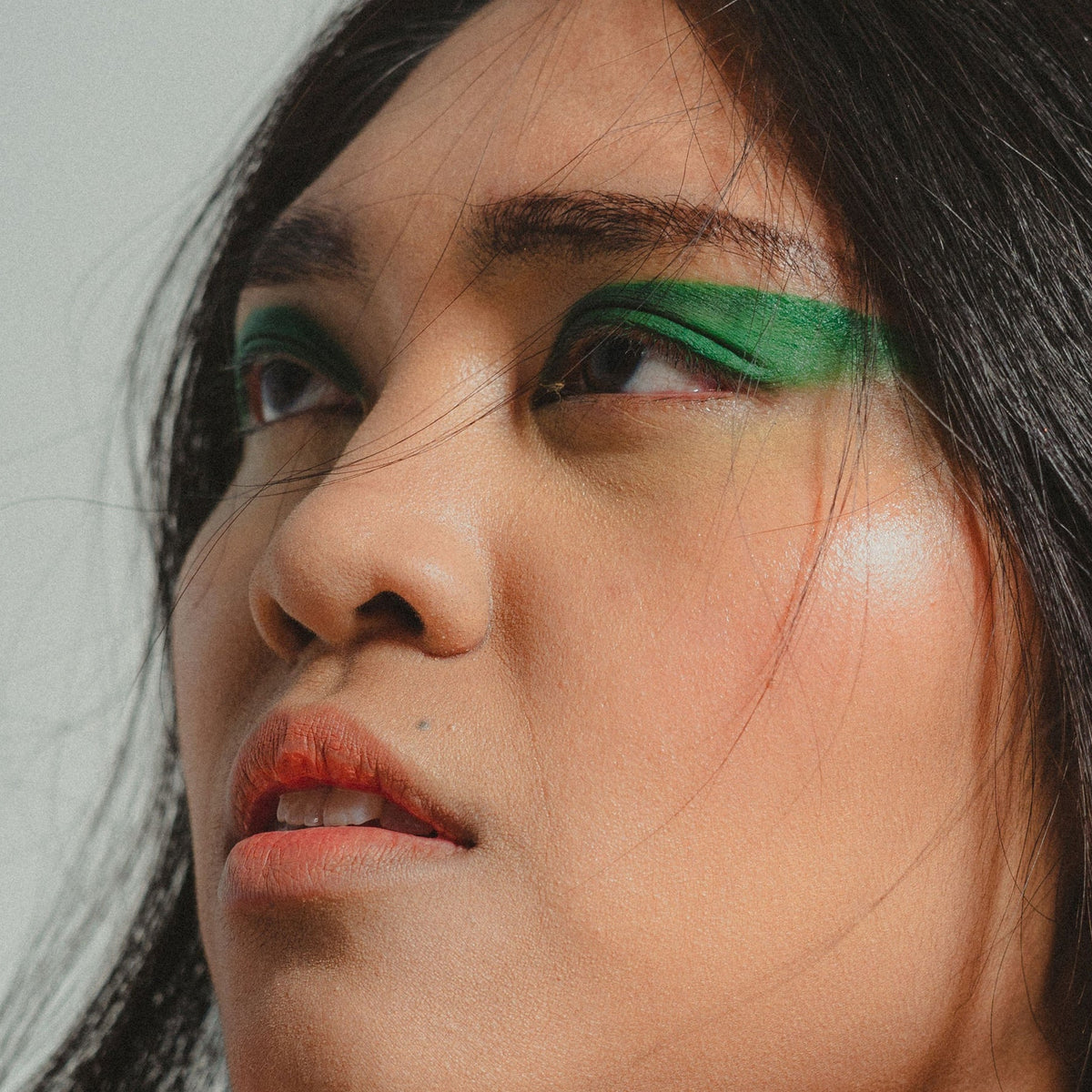 Close-up of a person with green eyeshadow and red lipstick against a neutral background. Makeup artist portfolio
