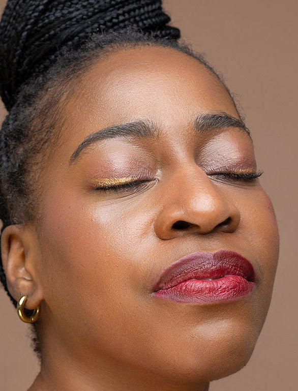 Woman with braided hair wearing gold earrings against a brown background