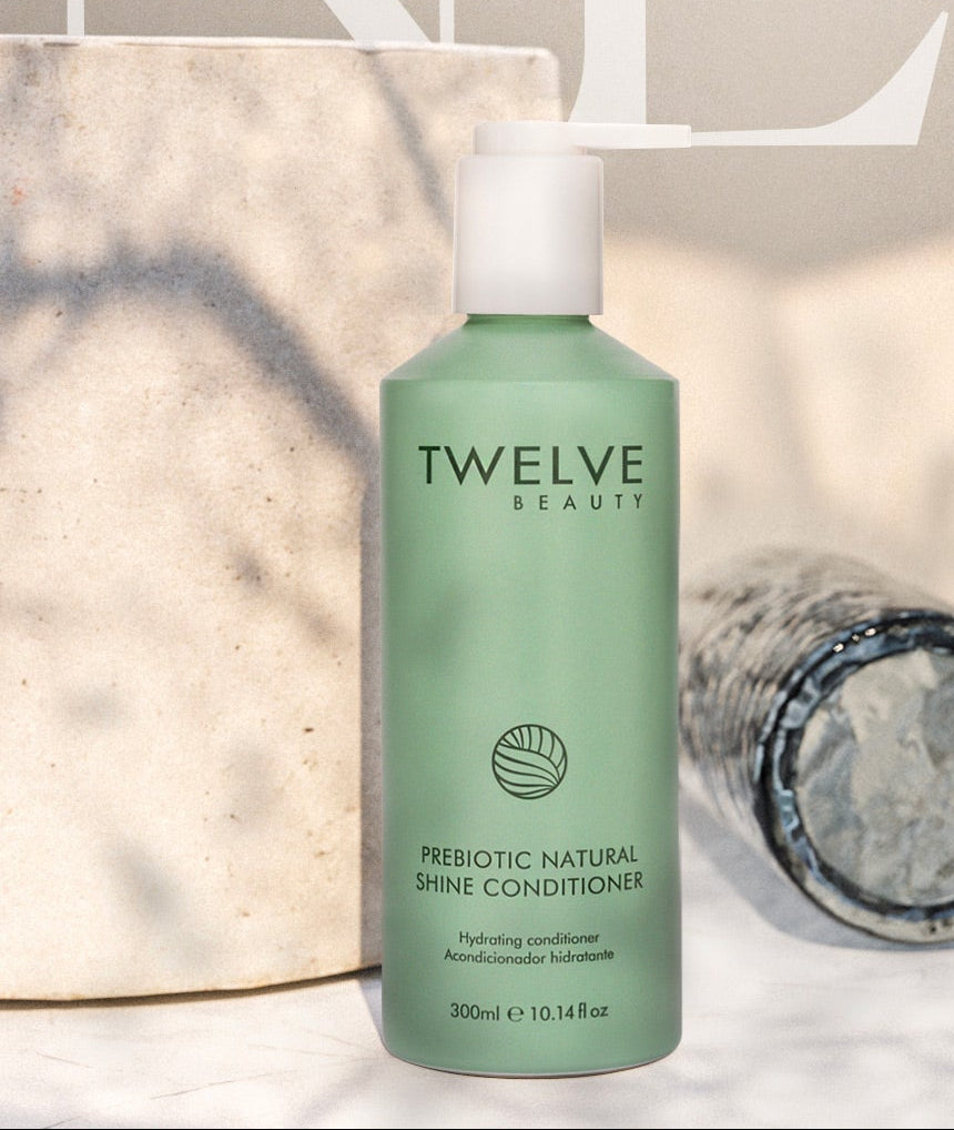 Two bottles of Twelve Beauty shampoo and conditioner on a textured surface with 'NEW' branding in the background.